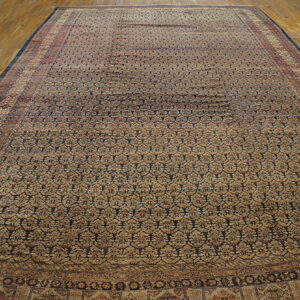Oversize rug with tan and dark blue repeating geometric patterns displayed on light hardwood floor.