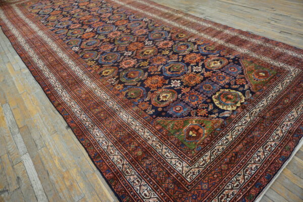 Long navy rug featuring complex orange and blue tribal motifs, framed by rust borders, on distressed wood.