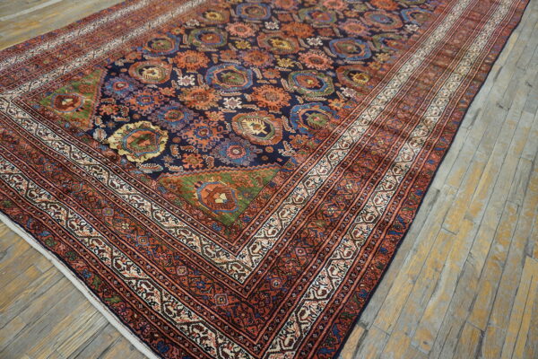 Angled view of a navy, rust, and cream rug with complex geometric patterns on weathered wood flooring.