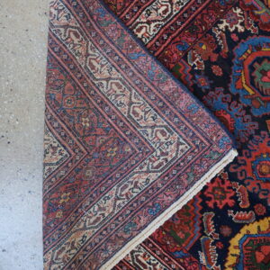 The woven underside of a navy, red, and beige patterned rug is visible as it is folded on concrete.