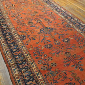 Orange runner rug featuring a deep blue stylized floral motif and wide patterned borders on wood flooring.