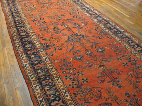 Orange runner rug featuring a deep blue stylized floral motif and wide patterned borders on wood flooring.