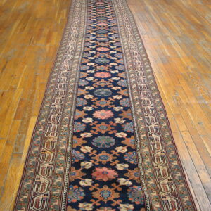 Dark blue runner rug featuring floral and geometric patterns in pink, rust, and teal on wooden floor.