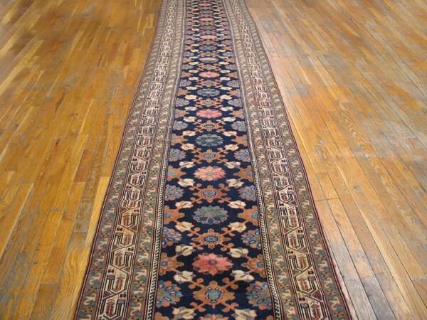 Dark blue runner rug featuring floral and geometric patterns in pink, rust, and teal on wooden floor.