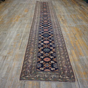 A long traditional runner rug with a navy floral pattern lies on distressed wood flooring.