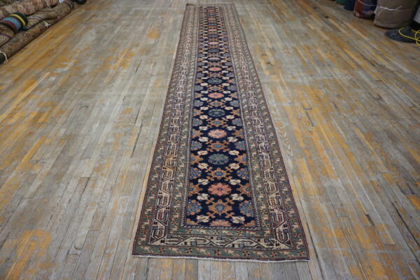 A long traditional runner rug with a navy floral pattern lies on distressed wood flooring.