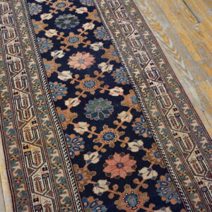 Navy floral runner rug with teal and coral details lies on worn, light wood floorboards.