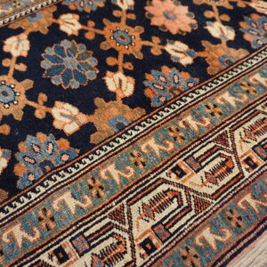 Low-pile rug in navy, rust, and teal features complex floral and geometric borders over wood flooring.