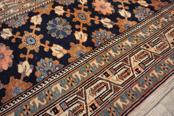 Low-pile rug in navy, rust, and teal features complex floral and geometric borders over wood flooring.
