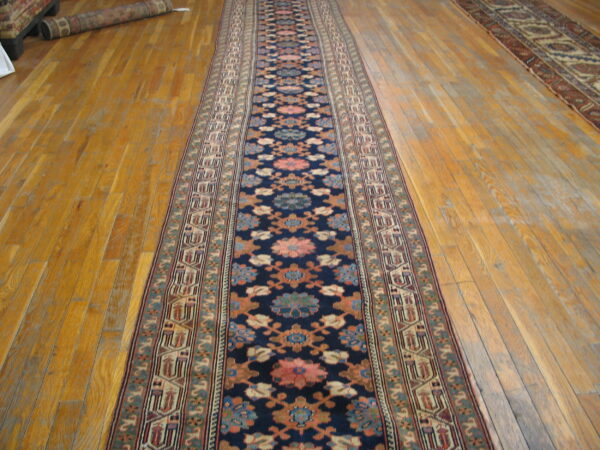 Dark blue runner rug with floral and geometric borders displayed on glossy wood planks.