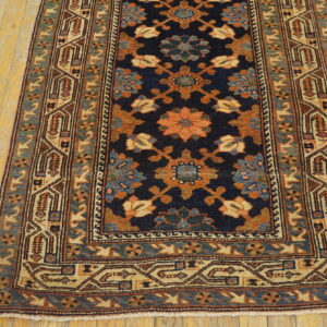 A low-pile navy runner rug with complex floral and geometric patterns rests on distressed yellow hardwood.