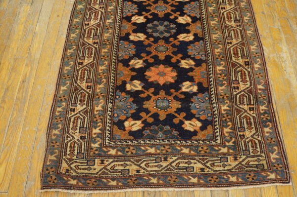 A low-pile navy runner rug with complex floral and geometric patterns rests on distressed yellow hardwood.