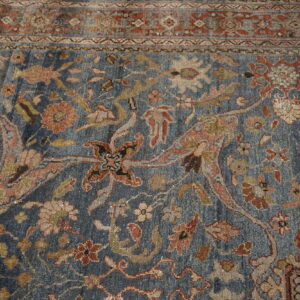 Detail of a faded blue rug showing a dense traditional floral pattern and a rust-toned border.