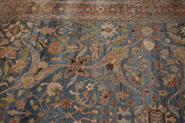 Detail of a faded blue rug showing a dense traditional floral pattern and a rust-toned border.