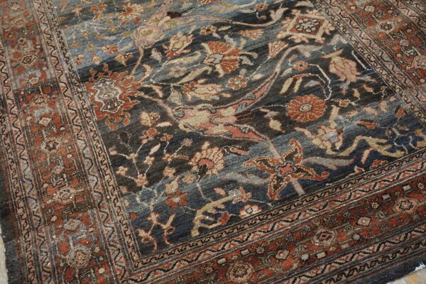 Traditional rug displaying dark blue, grey, and terracotta floral patterns with complex borders.