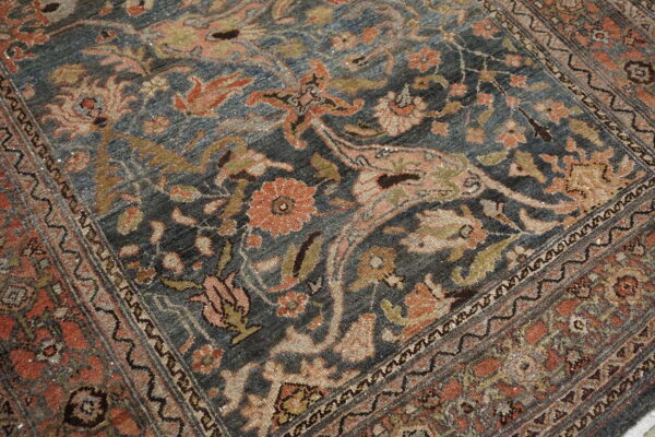 Close-up of a rug featuring a faded navy blue field with detailed terracotta, beige, and olive floral motifs.