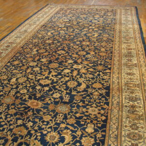 A large navy blue rug with an intricate gold floral pattern and tan borders rests on hardwood floors.