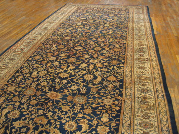 A large navy blue rug with an intricate gold floral pattern and tan borders rests on hardwood floors.
