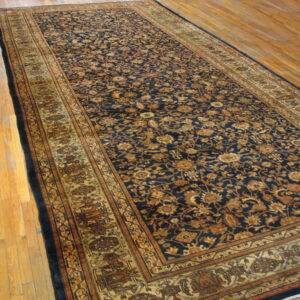 Long dark blue runner rug with gold and brown floral pattern lying on light hardwood flooring.