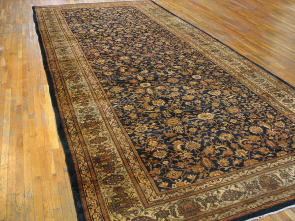 Long dark blue runner rug with gold and brown floral pattern lying on light hardwood flooring.