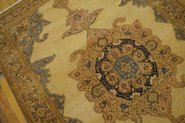 Traditional yellow area rug displaying complex floral patterns, a dark blue medallion center, and brown borders on wood floor.
