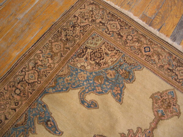 Low-pile rug corner showing tan field, detailed brown and pink borders, and blue patterns on distressed wood planks.