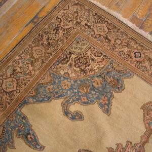 Low pile tan rug featuring intricate patterns in brown, peach, and blue resting on distressed wood flooring.