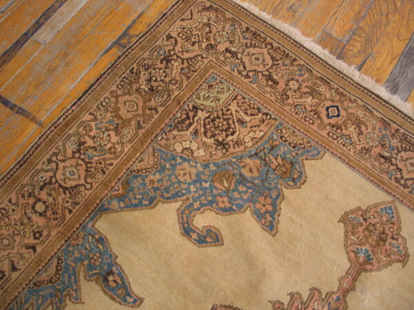 Low pile tan rug featuring intricate patterns in brown, peach, and blue resting on distressed wood flooring.