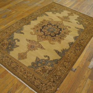 Low-pile rug with a detailed central medallion in camel, indigo, and rust on worn hardwood flooring.