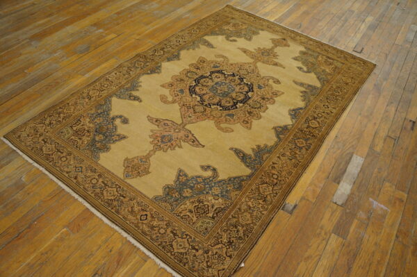 Low-pile rug with a detailed central medallion in camel, indigo, and rust on worn hardwood flooring.