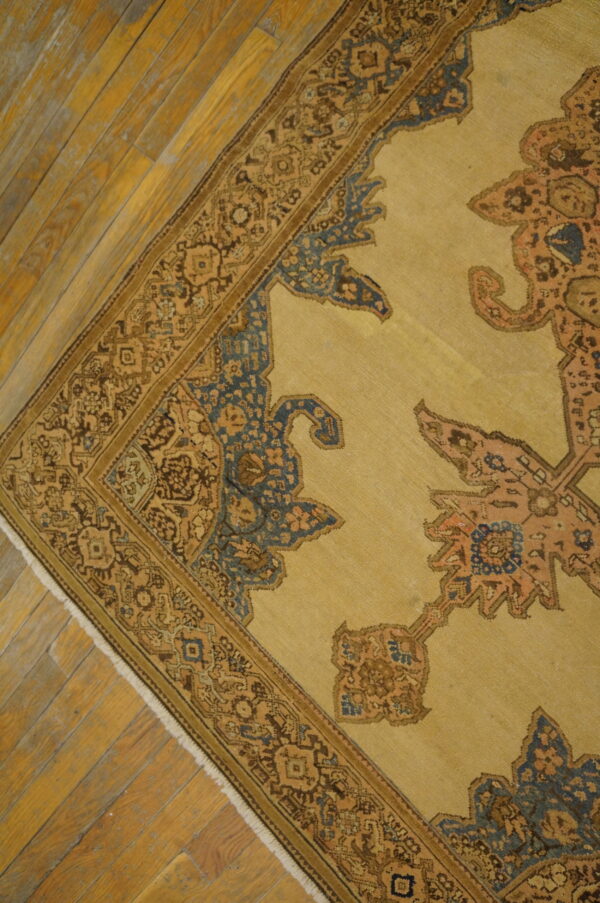 Close-up of a traditional tan and brown rug featuring blue accents on distressed wood flooring.