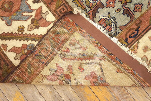 A multicolored rug is folded to reveal its woven backing, a brown pad, and distressed wood floorboards.