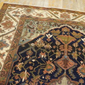 Traditional rug featuring a navy field, ivory border, and rust/green patterns on distressed wooden plank floor.