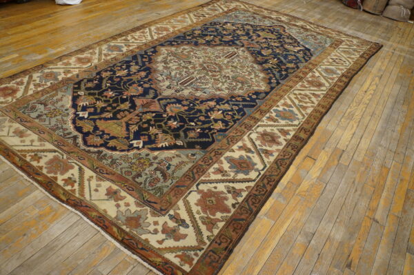 Blue and cream patterned rug with rust and sage accents lies diagonally on light brown wood flooring.