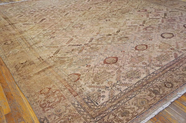 Tan area rug with faded geometric patterns in brown and rust, laid on hardwood flooring.