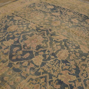 Ornate, faded blue and gold floral rug with pink accents covers a worn wooden plank floor.