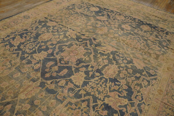 Ornate, faded blue and gold floral rug with pink accents covers a worn wooden plank floor.