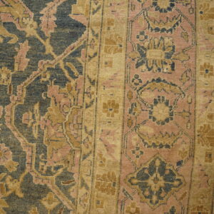 Ornate, faded blue and gold floral rug with pink accents covers a worn wooden plank floor.