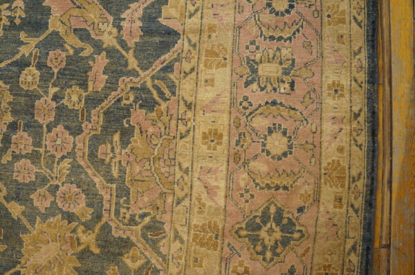 Ornate, faded blue and gold floral rug with pink accents covers a worn wooden plank floor.