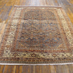 Traditional blue and tan patterned rug with fringes covers rustic, wide plank wooden flooring.