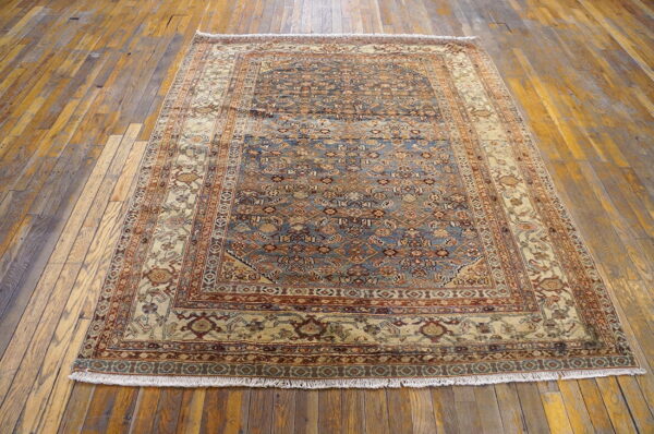 Traditional blue and tan patterned rug with fringes covers rustic, wide plank wooden flooring.