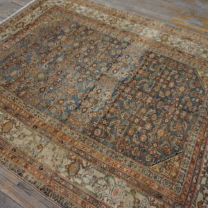 A distressed traditional rug in muted blue, rust, and beige rests on rustic gray plank flooring.