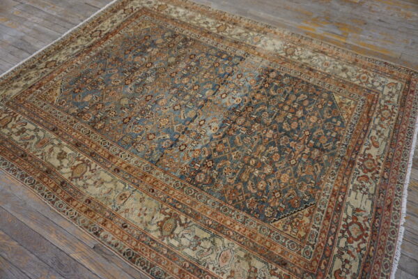 A distressed traditional rug in muted blue, rust, and beige rests on rustic gray plank flooring.