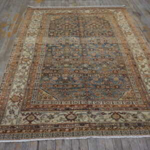 A patterned rug with a blue center field and cream border rests on rustic gray wooden floorboards.