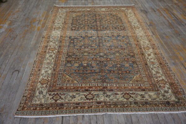 A patterned rug with a blue center field and cream border rests on rustic gray wooden floorboards.