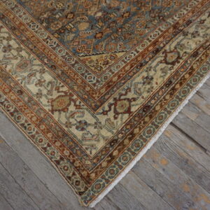 Overhead view of a detailed beige, rust, and blue patterned rug corner on weathered gray floorboards.