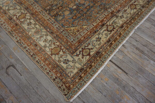 Overhead view of a detailed beige, rust, and blue patterned rug corner on weathered gray floorboards.