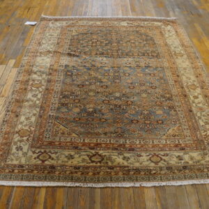 Traditional blue, rust, and cream patterned rug with fringe displayed on rustic light brown hardwood flooring.