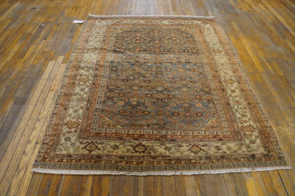 Traditional blue, rust, and cream patterned rug with fringe displayed on rustic light brown hardwood flooring.