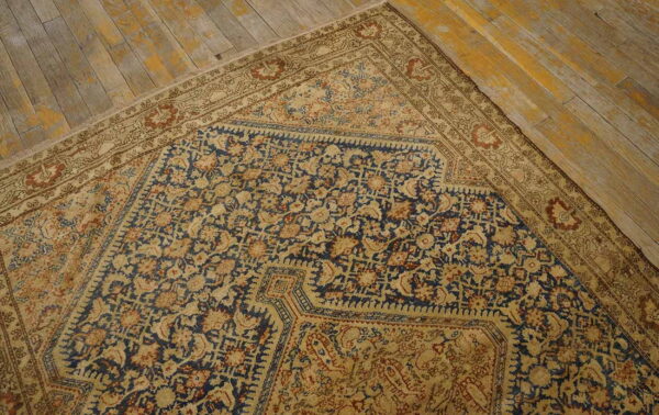 Corner view of a traditional navy and beige patterned rug on distressed wooden planks.